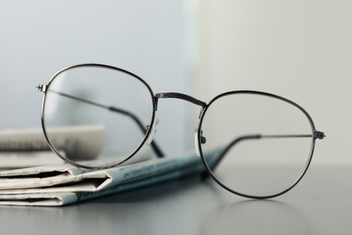 Photo of Stack of newspapers and glasses on grey table indoors, closeup