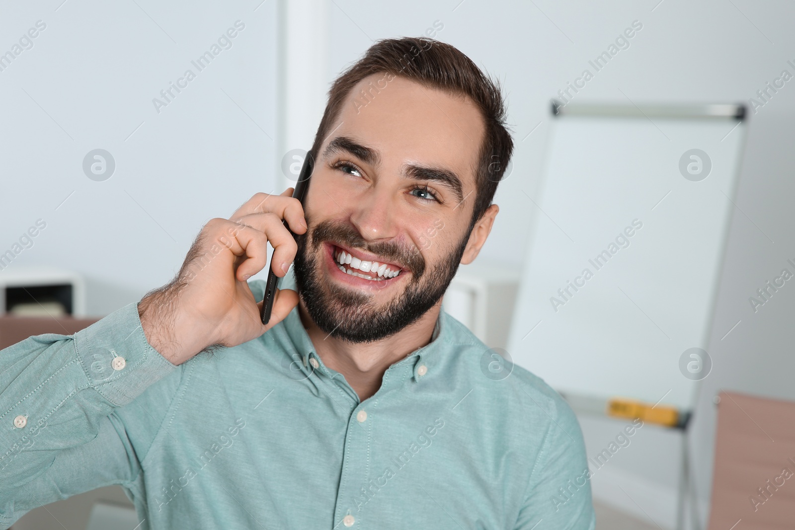 Photo of Young man laughing while talking on phone in office