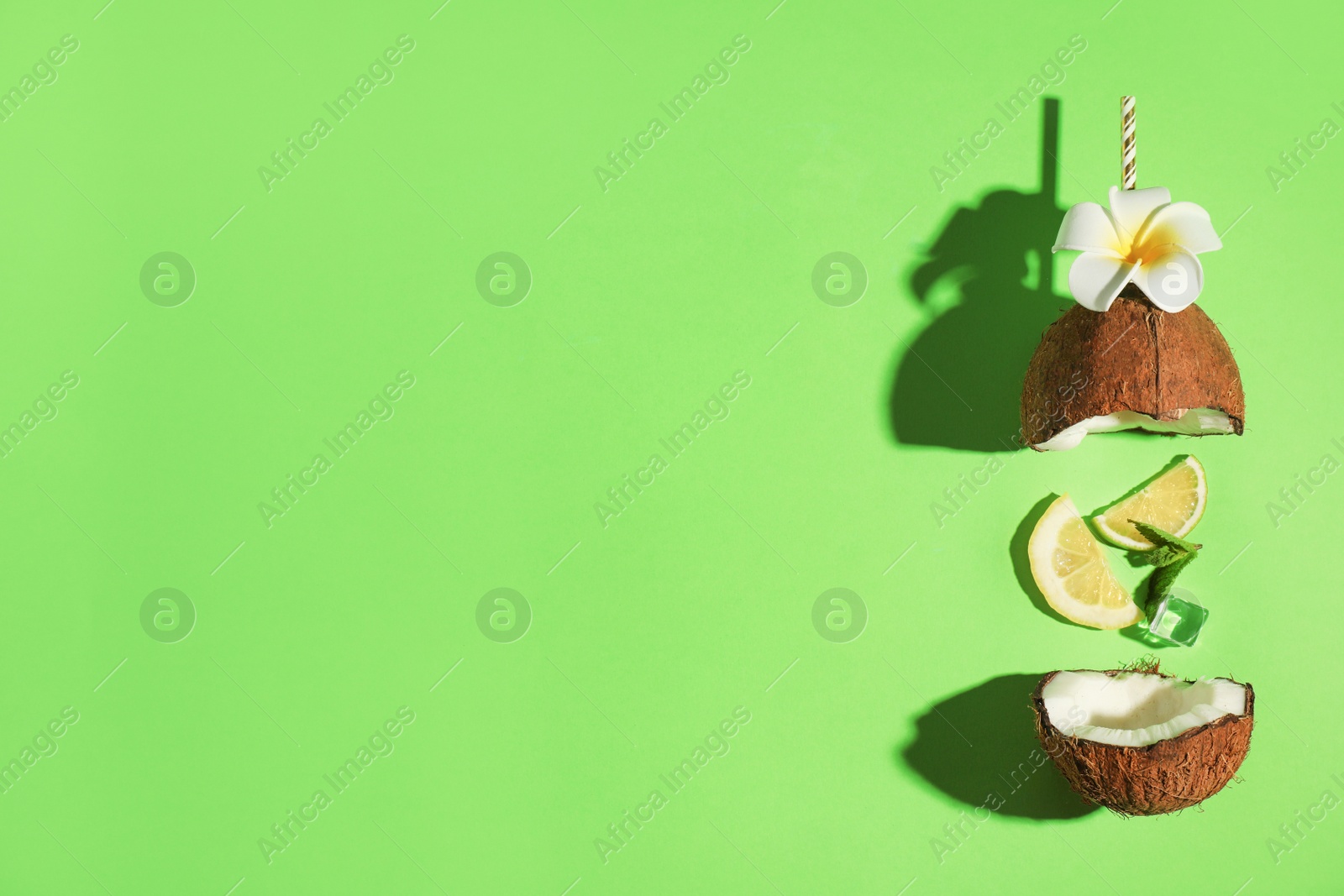 Photo of Creative image of summer cocktail made with coconut, lemon slice, mint, ice and straw on green background, top view. Space for text