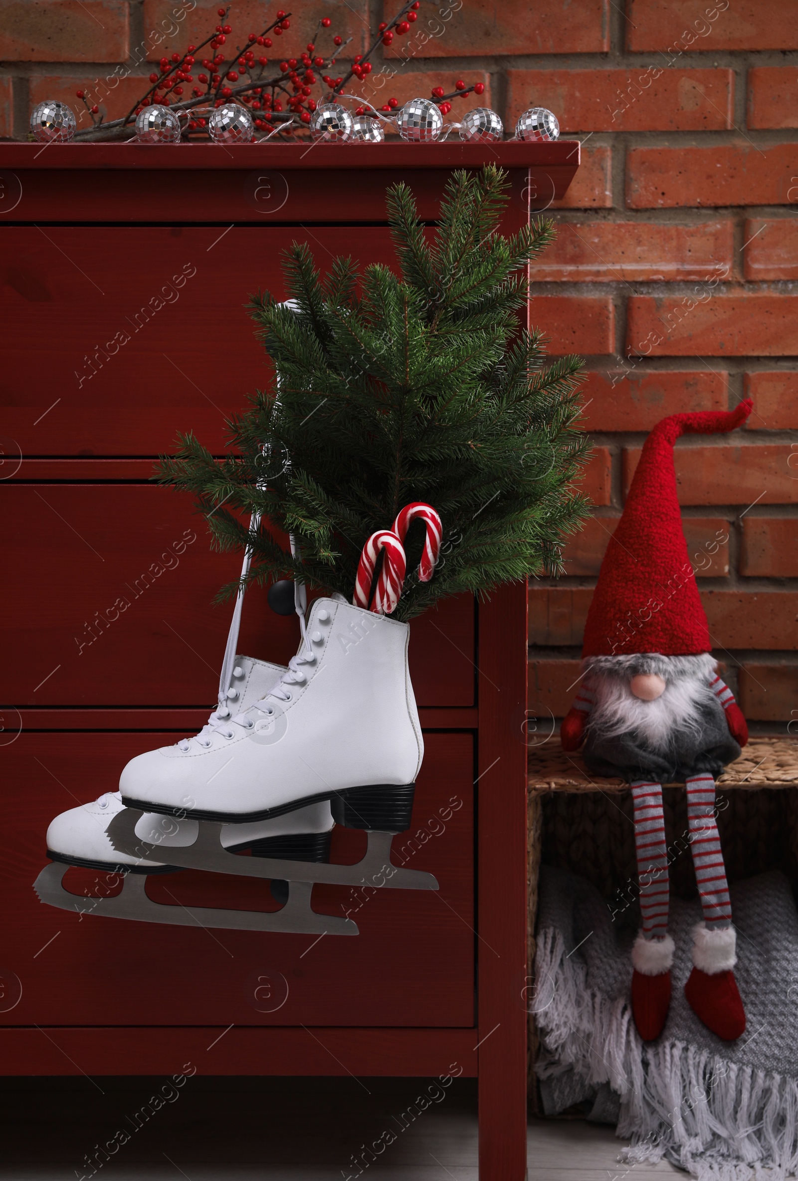 Photo of Pair of ice skates with Christmas decor hanging on red wooden cabinet indoors