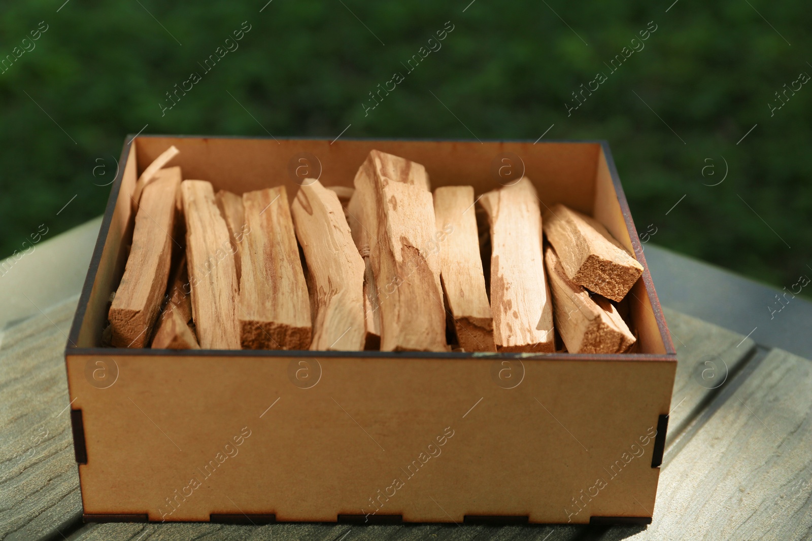 Photo of Box of many palo santo sticks on wooden table outdoors