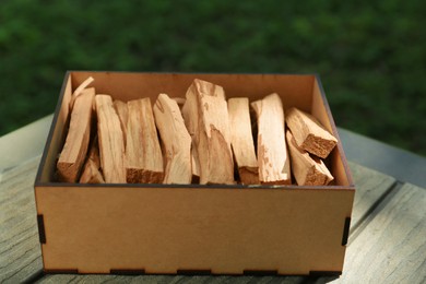Photo of Box of many palo santo sticks on wooden table outdoors