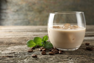 Photo of Coffee cream liqueur in glass, mint and beans on wooden table, closeup. Space for text