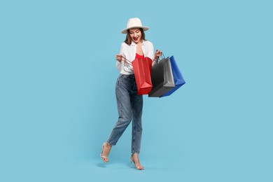 Photo of Stylish young woman with shopping bags on light blue background. Space for text