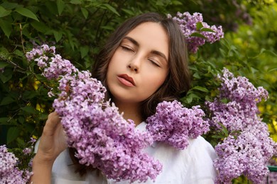 Attractive young woman near blooming lilac bush outdoors