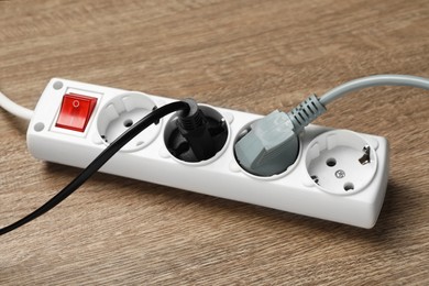 Photo of Power strip with extension cord on wooden floor, closeup. Electrician's equipment