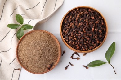 Photo of Aromatic clove powder and dried buds in bowls on white table, flat lay