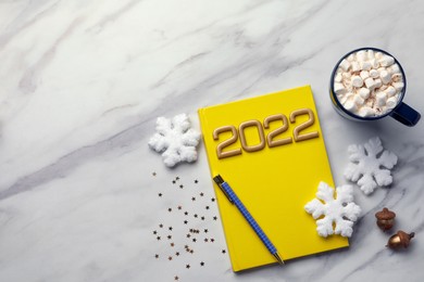 Photo of Stylish planner, cup of tasty hot drink and Christmas decor on white marble background, flat lay with space for text. 2022 New Year aims