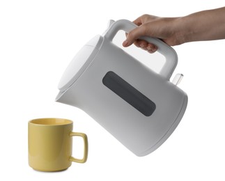 Woman pouring hot water from electric kettle into cup on white background, closeup