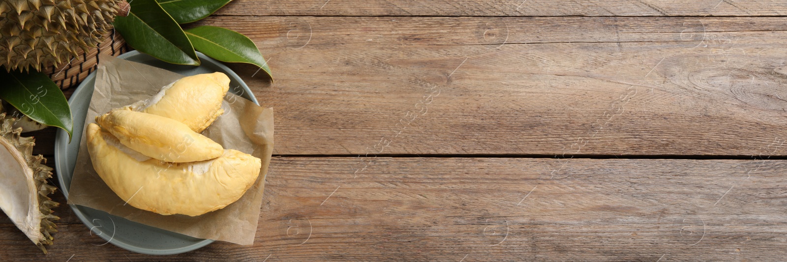 Image of Fresh ripe durians and leaves on wooden table, flat lay with space for text. Banner design