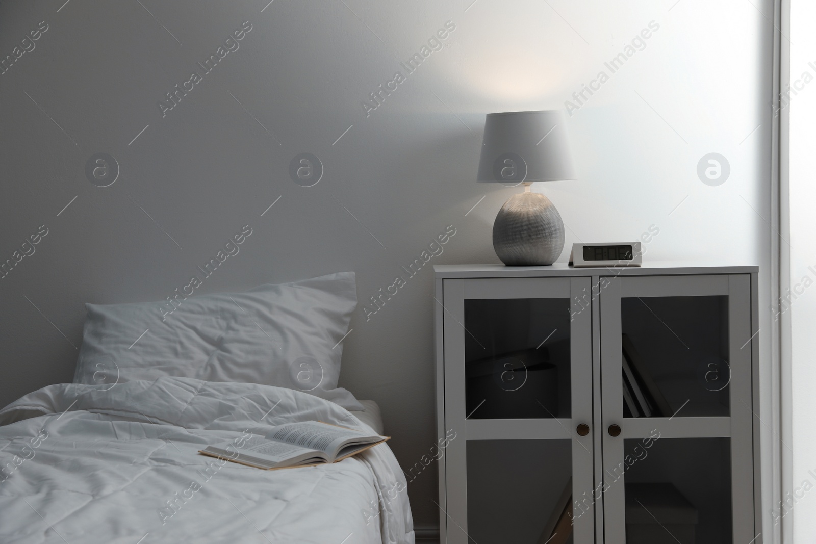 Photo of Stylish lamp and alarm clock on bedside table indoors. Bedroom interior elements