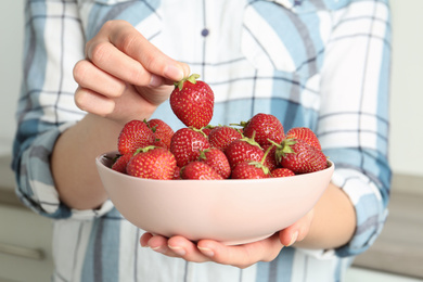 Woman holding bowl with tasty fresh strawberries indoors, closeup