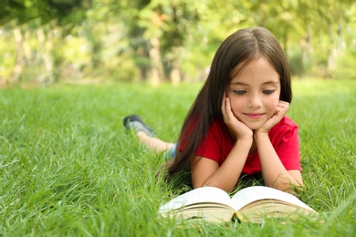 Photo of Cute little girl reading book on green grass in park