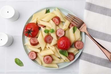 Photo of Tasty pasta with smoked sausage, tomatoes and basil served on white tiled table, flat lay