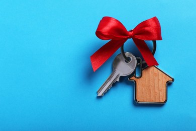 Photo of Key with trinket in shape of house and bow on light blue background, top view. Space for text. Housewarming party