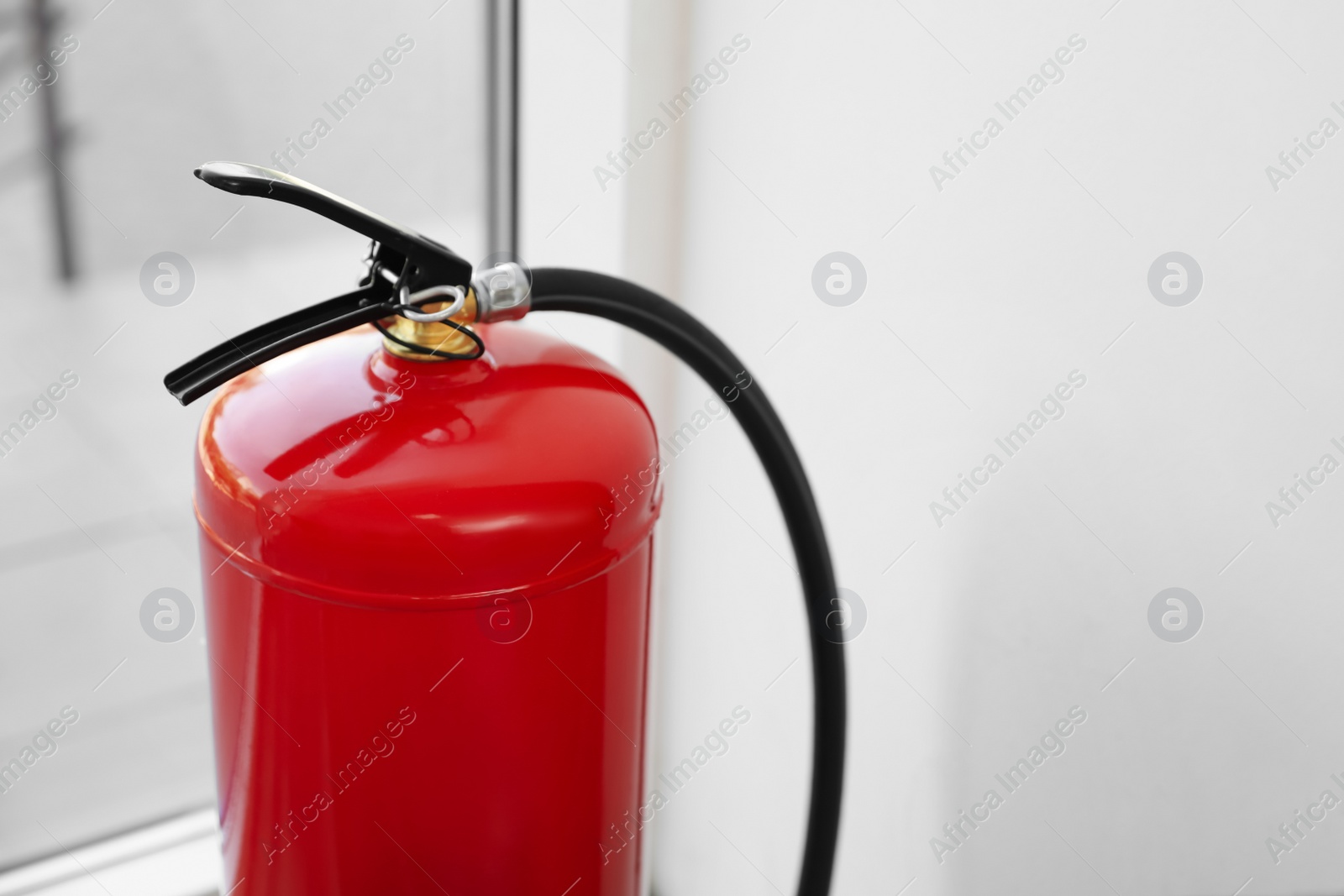 Photo of Fire extinguisher near window indoors, closeup. Space for text