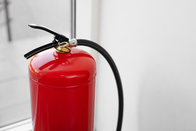 Fire extinguisher near window indoors, closeup. Space for text
