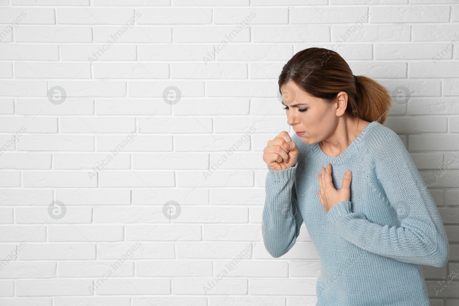 Photo of Woman suffering from cough near brick wall. Space for text