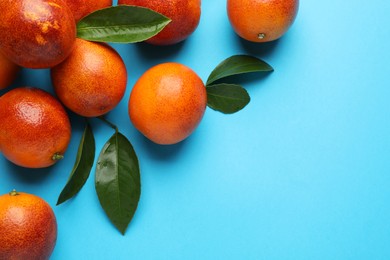 Photo of Many ripe sicilian oranges and leaves on light blue background, flat lay. Space for text