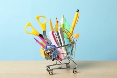 Photo of Small cart with different school stationery on wooden table against light blue background. Back to school