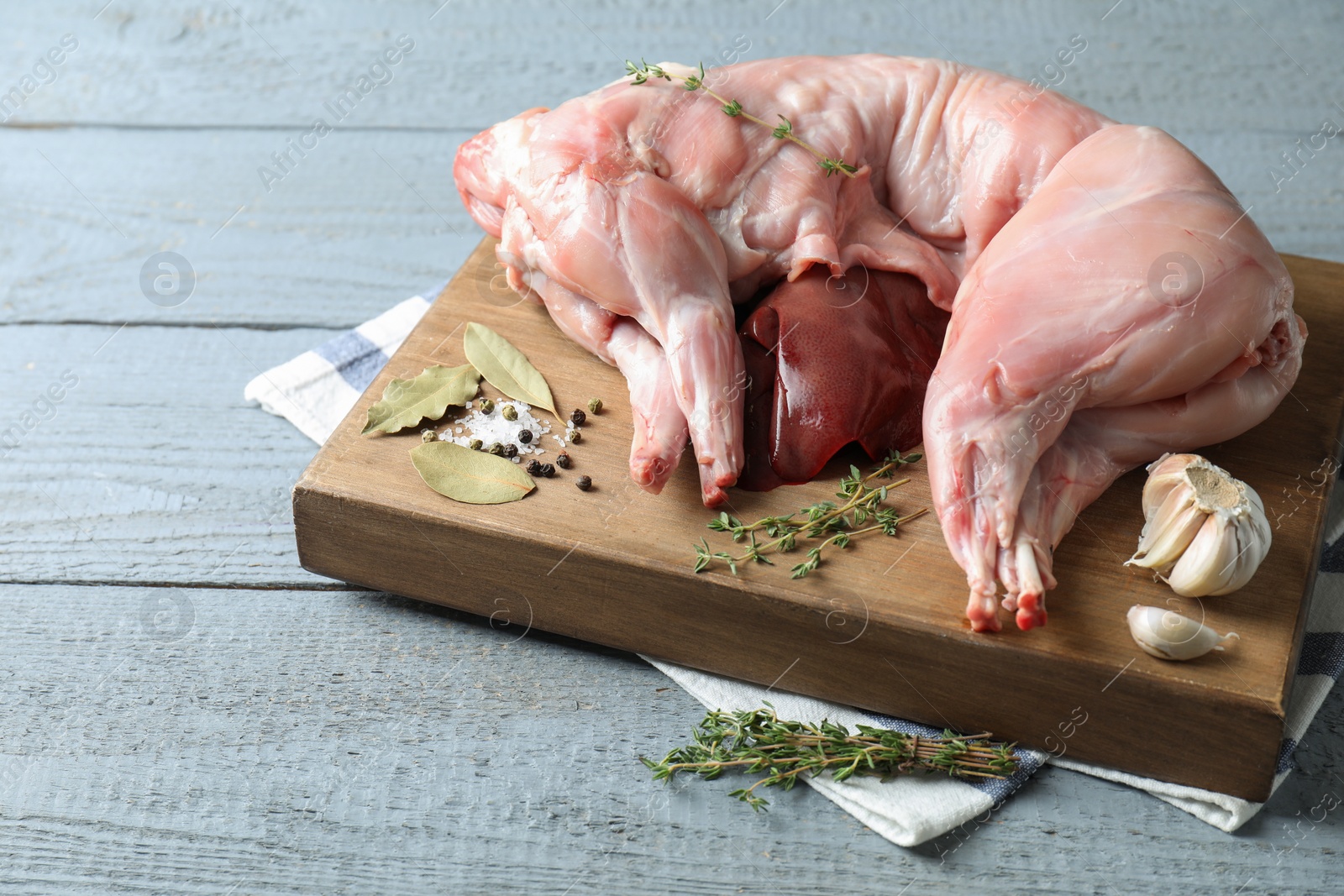 Photo of Whole raw rabbit, liver and spices on grey wooden table, space for text