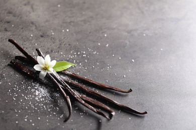 Vanilla pods, flower, leaf and sugar on grey textured table, closeup. Space for text