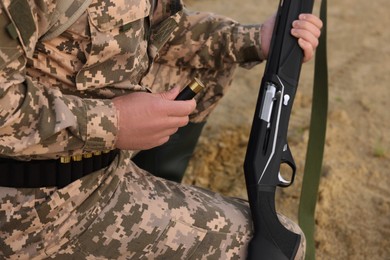 Photo of Man wearing camouflage with hunting rifle and cartridge outdoors, closeup