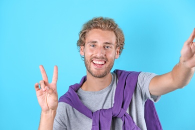 Photo of Handsome young man laughing and taking selfie on color background