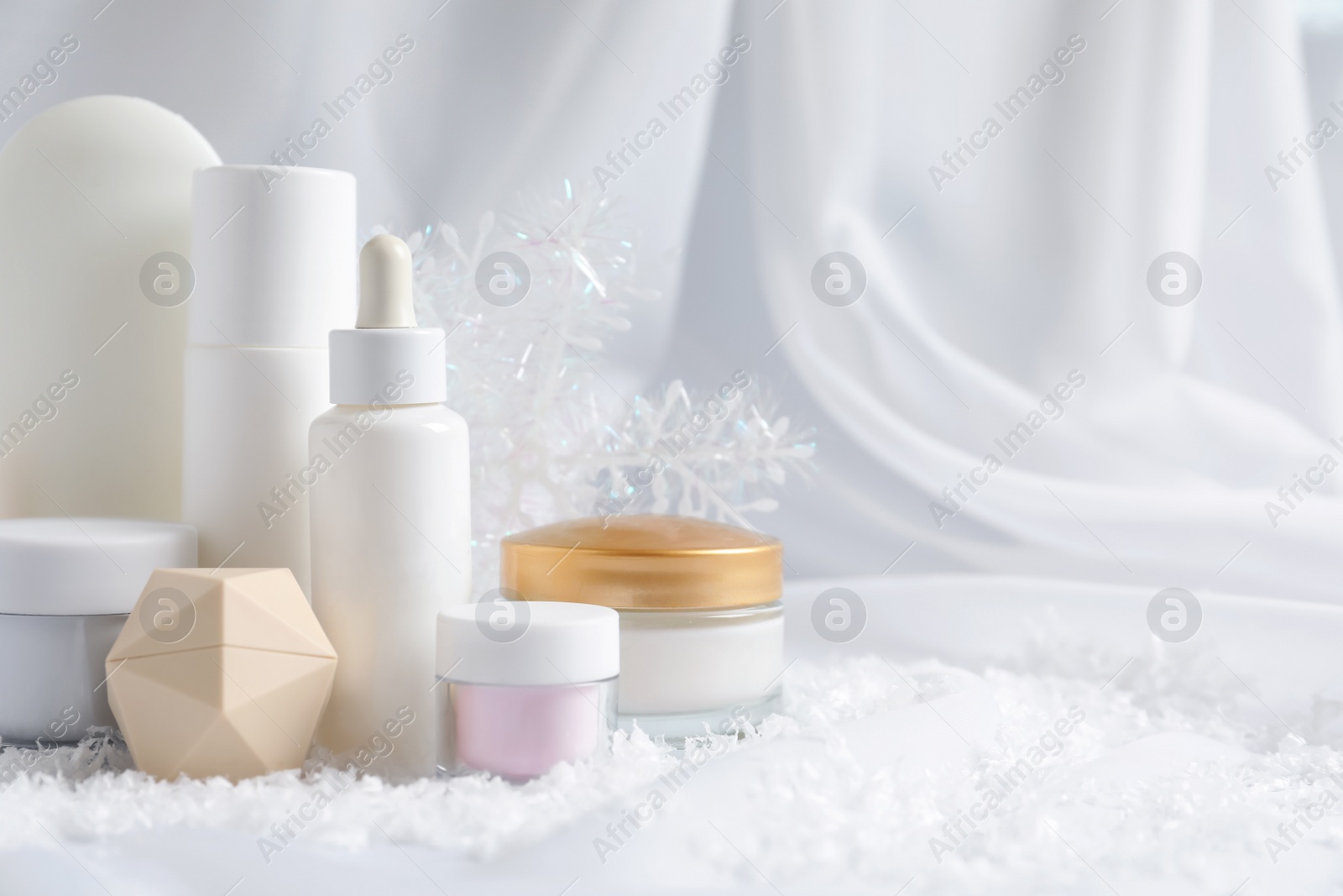 Photo of Set of cosmetic products and decorative snow on white fabric, space for text. Winter care