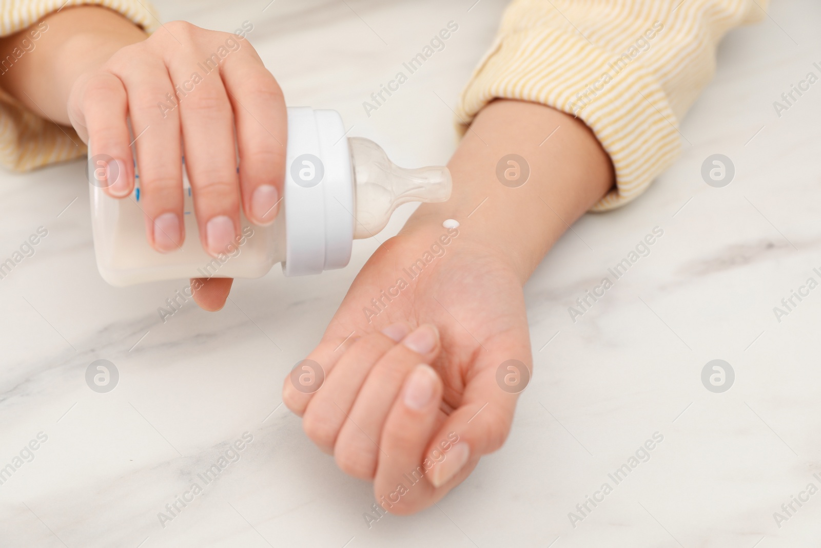 Photo of Woman checking infant formula temperature at white table, closeup. Baby milk