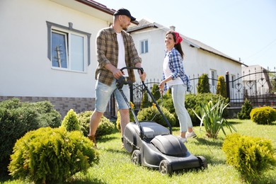 Happy couple spending time together while cutting green grass with lawn mower in garden