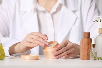 Dermatologist with jar testing cosmetic product at white table, selective focus