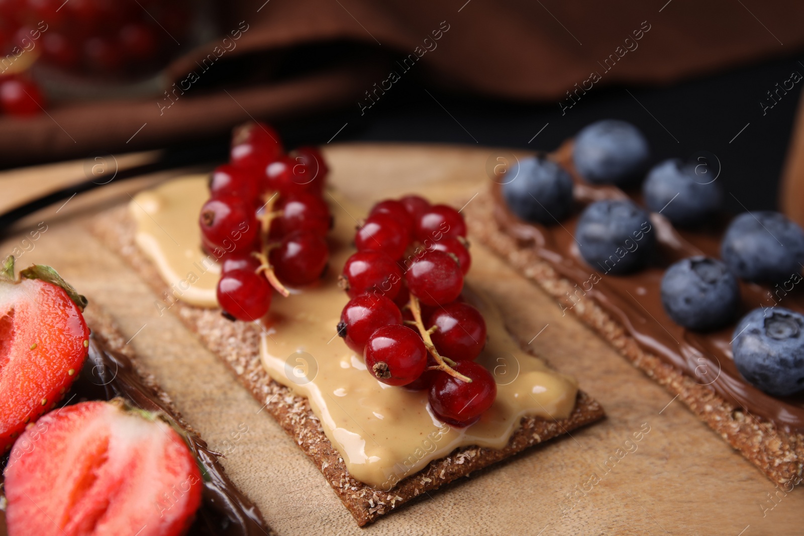 Photo of Fresh crunchy rye crispbreads with different toppings on wooden board, closeup