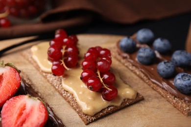 Photo of Fresh crunchy rye crispbreads with different toppings on wooden board, closeup