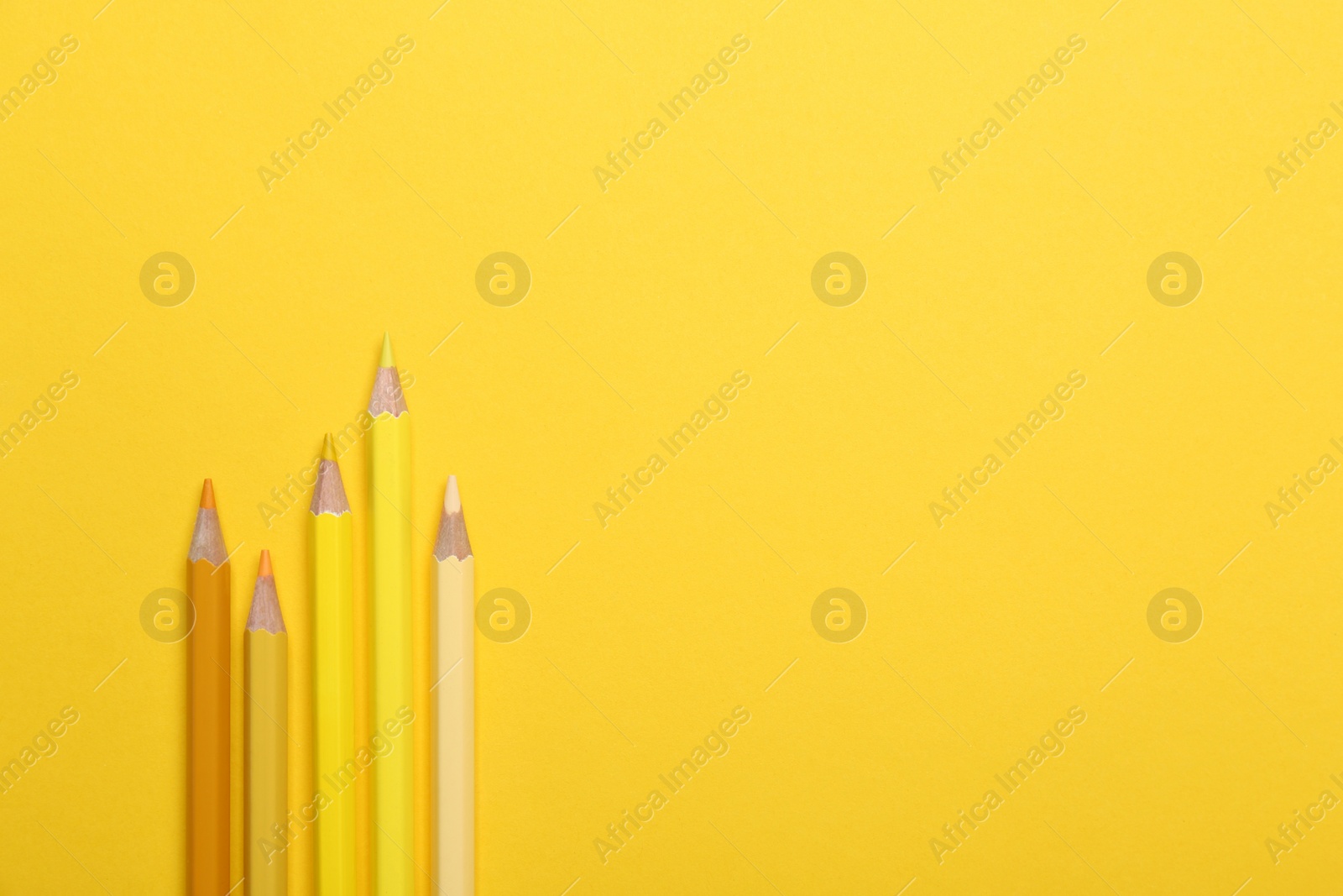 Photo of Color pencils on yellow background, flat lay. Space for text