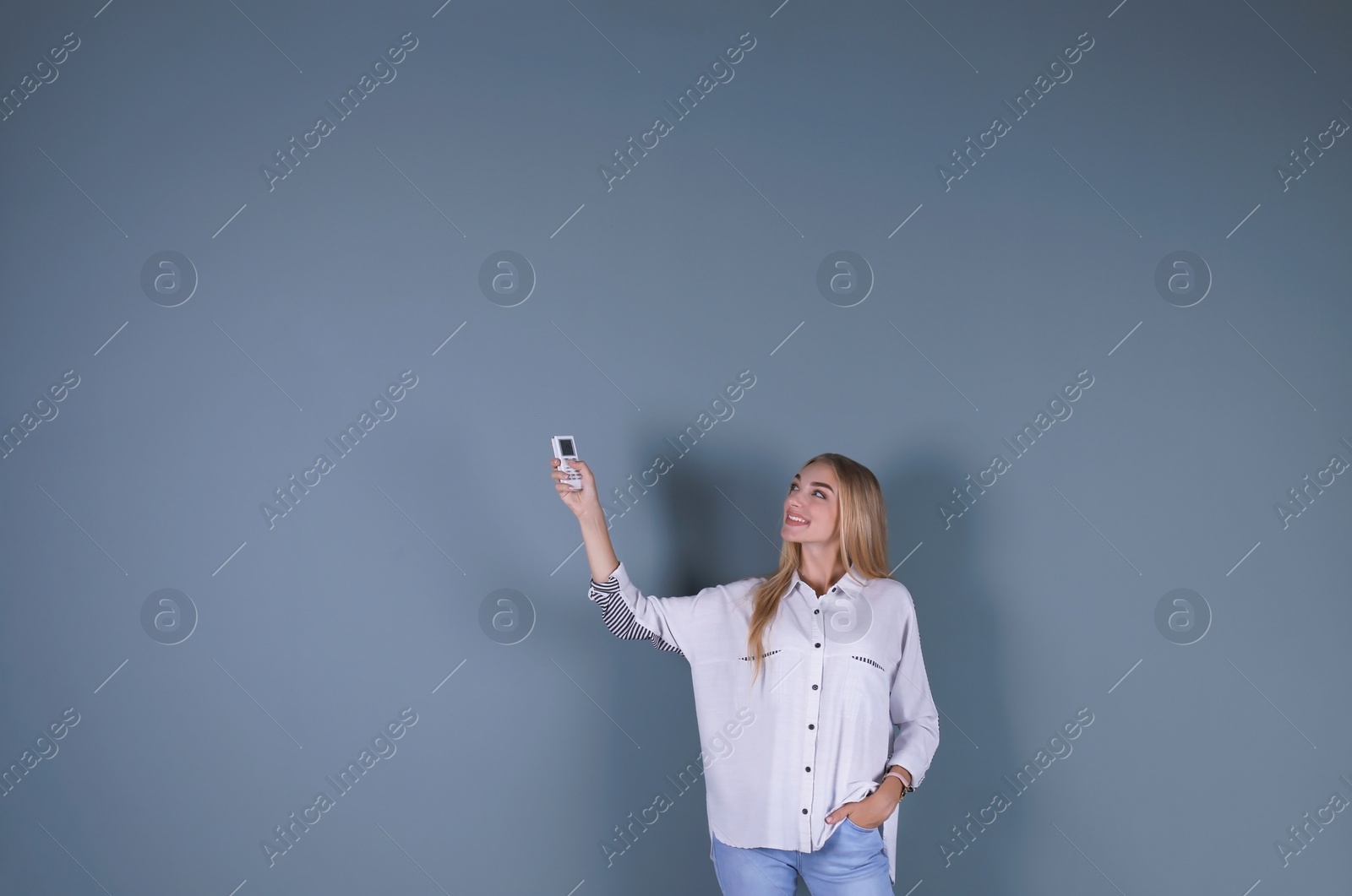 Photo of Young woman operating air conditioner with remote control on color background