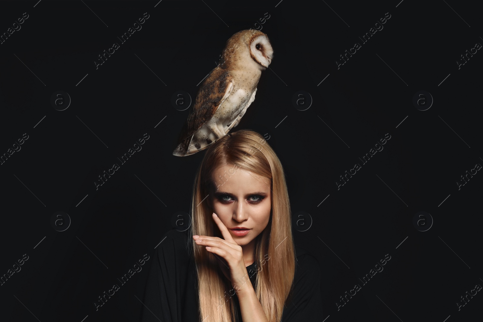 Photo of Witch in black mantle with owl on dark background. Scary fantasy character