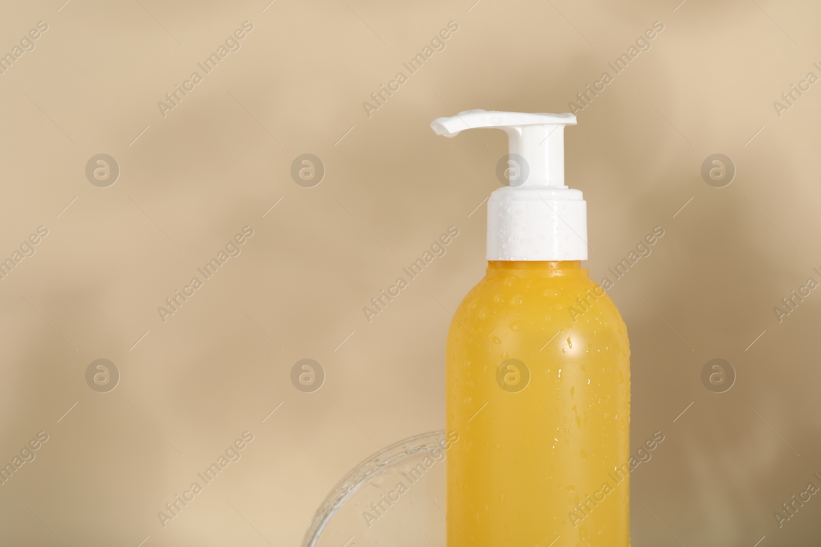 Photo of Wet bottle of facial cleanser on beige background, closeup. Space for text