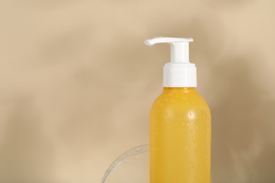 Wet bottle of facial cleanser on beige background, closeup. Space for text