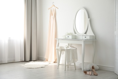 Beautiful wedding gown hanging near dressing table in room