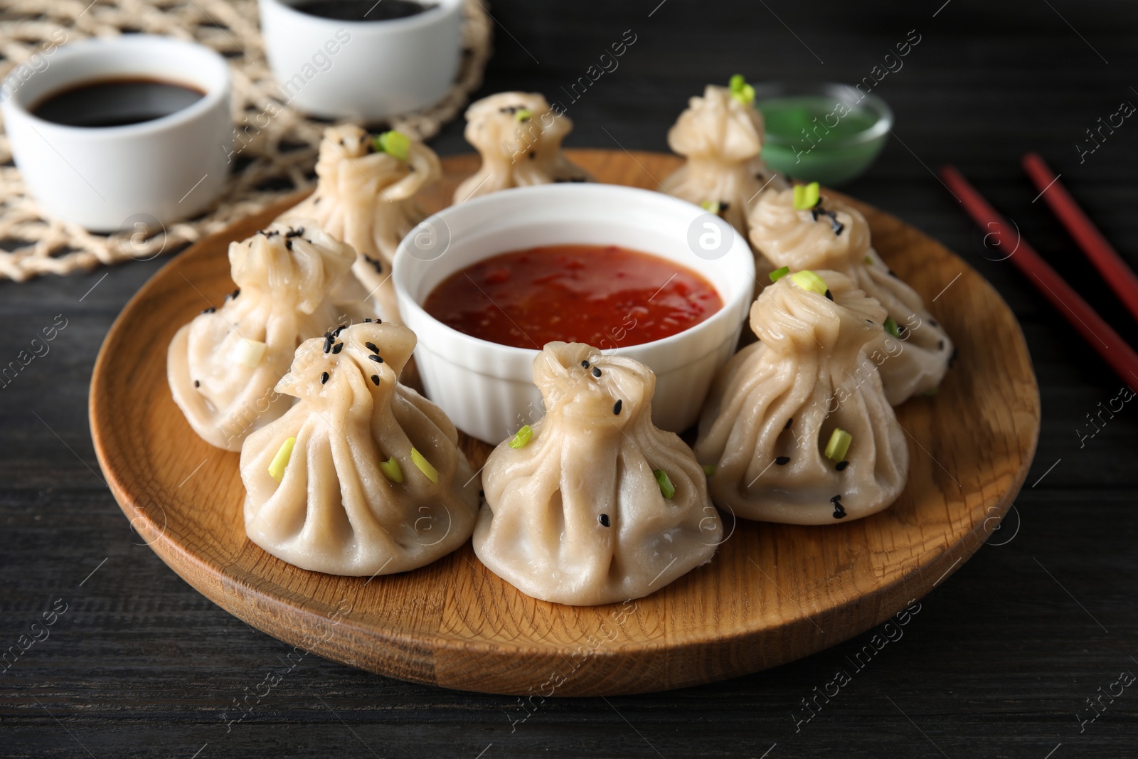 Photo of Wooden plate with tasty baozi dumplings and sauce on table