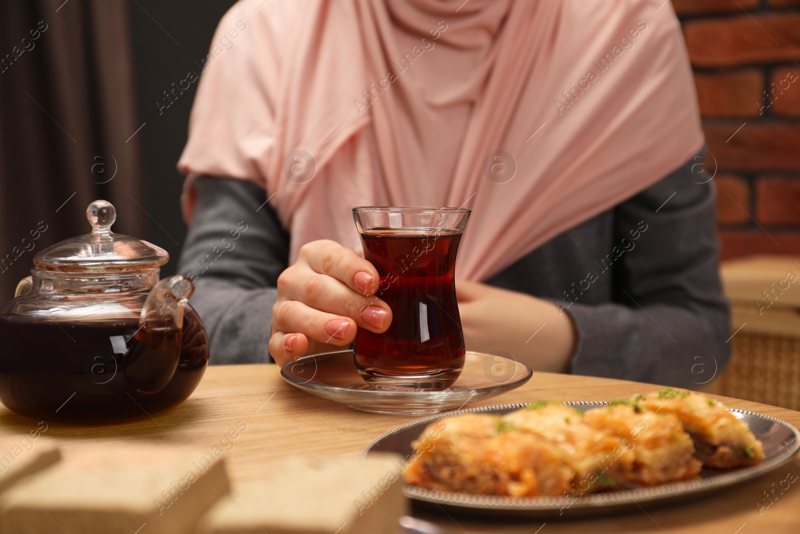 Photo of Woman with cup of delicious Turkish tea at wooden table, closeup