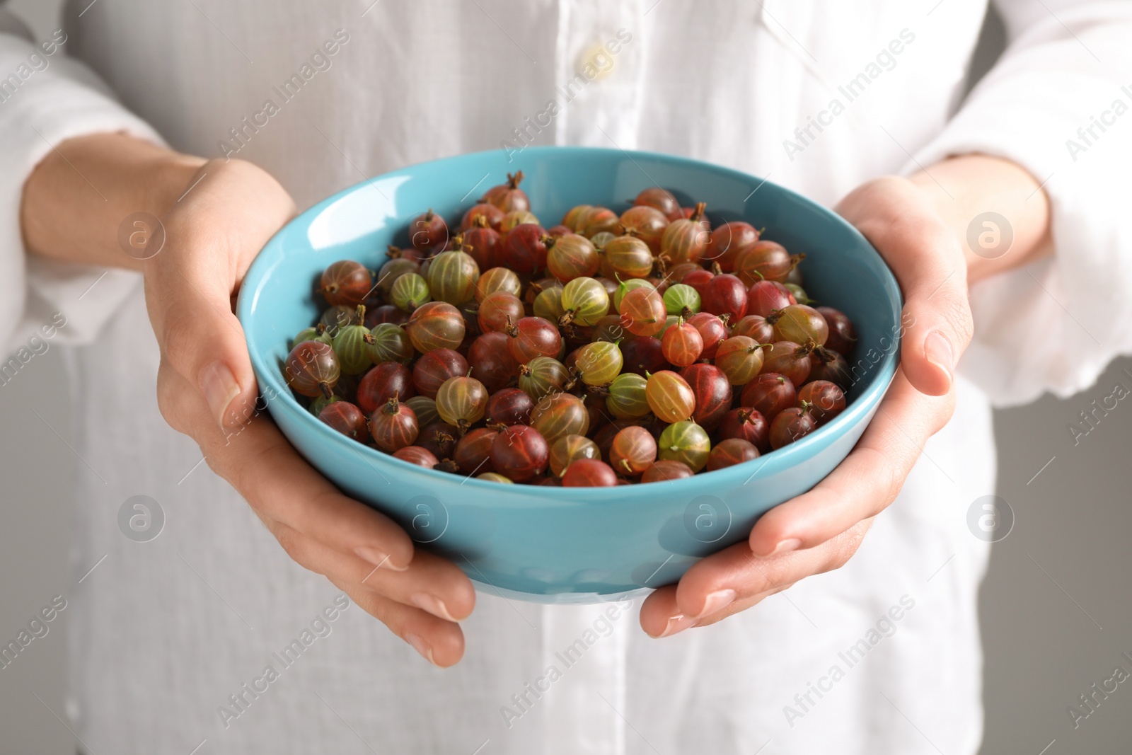 Photo of Woman holding bowl full of ripe gooseberries, closeup