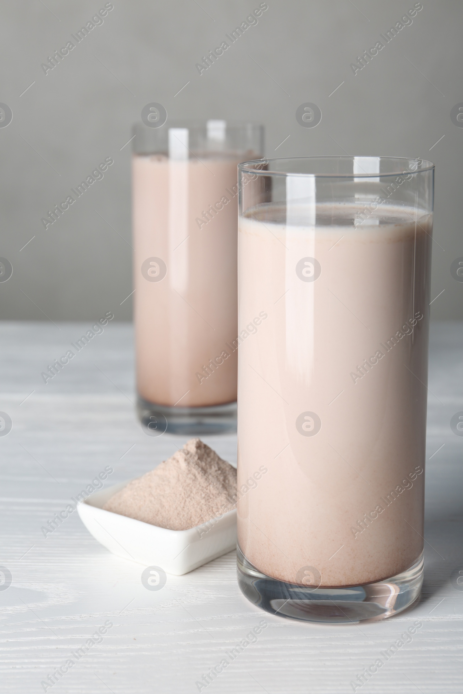 Photo of Glasses with protein shake and bowl of powder on white wooden table