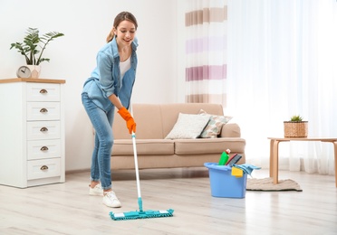 Photo of Young woman washing floor with mop in living room. Cleaning service