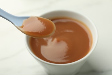 Photo of Eating healthy baby food with spoon at white table, closeup