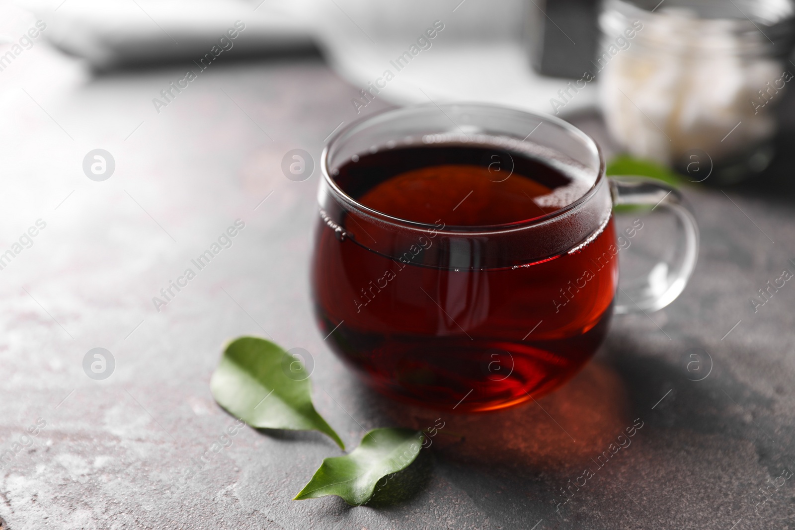 Photo of Tasty hot tea in cup and leaves on grey table, closeup. Space for text