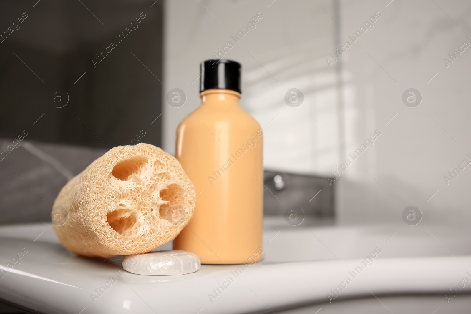 Photo of Natural loofah sponge and shower gel bottle on washbasin in bathroom, space for text