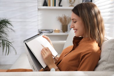 Photo of Young woman drawing in sketchbook with pencil at home