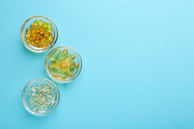 Different vitamin capsules in bowls on light blue background, flat lay. Space for text